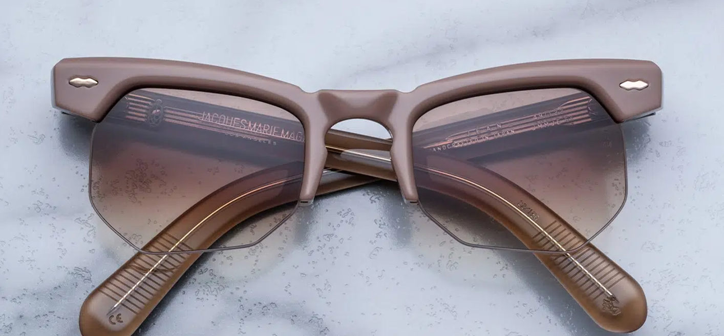 Front view of Jacques Marie Mage Jean sunglasses in Porter, featuring a semi-rimless construction with exaggerated brow lines. Crafted from nude 10mm cured cellulose acetate, the frame showcases signature light gold double arrowhead pins and an inner wirecore. The sand gradient 6-base CR39 lenses offer 100% UV protection and backside anti-reflective treatment.