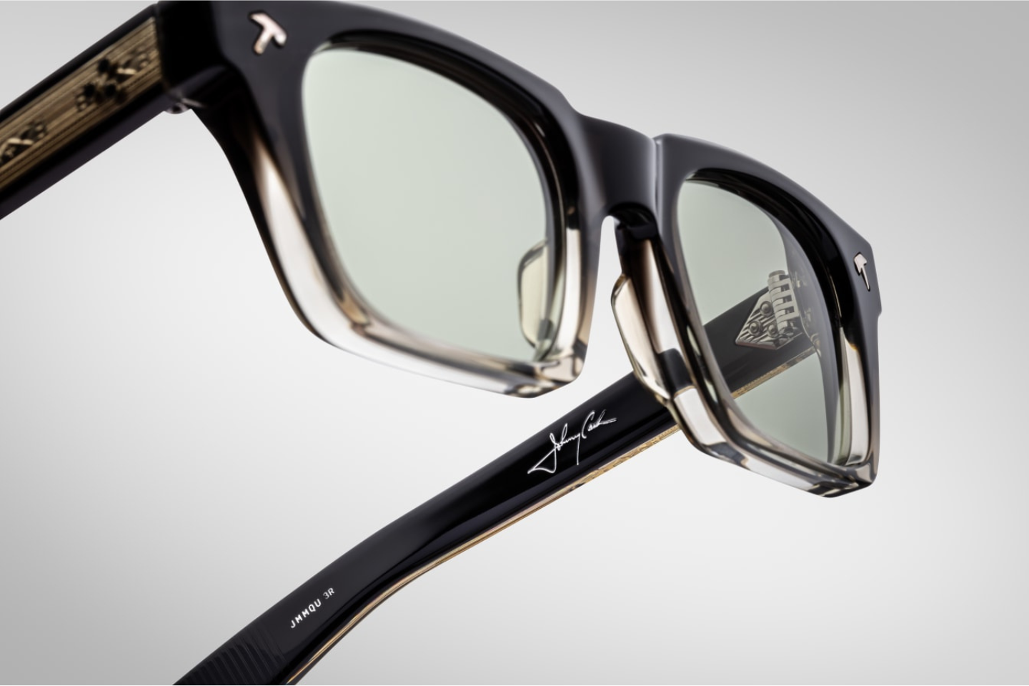 Jacques Marie Mage Quentin Black Fade sunglasses from the Johnny Cash collection. The side view reveals an exposed, engraved silver spike tail wire-core set into the temple’s lamination, secured with a tension secured 9-barrel hinge and sterling silver hatchet-shaped front pin. The lenses are lightly tinted green Serpent Amorlite CR39 with full UV protection. 