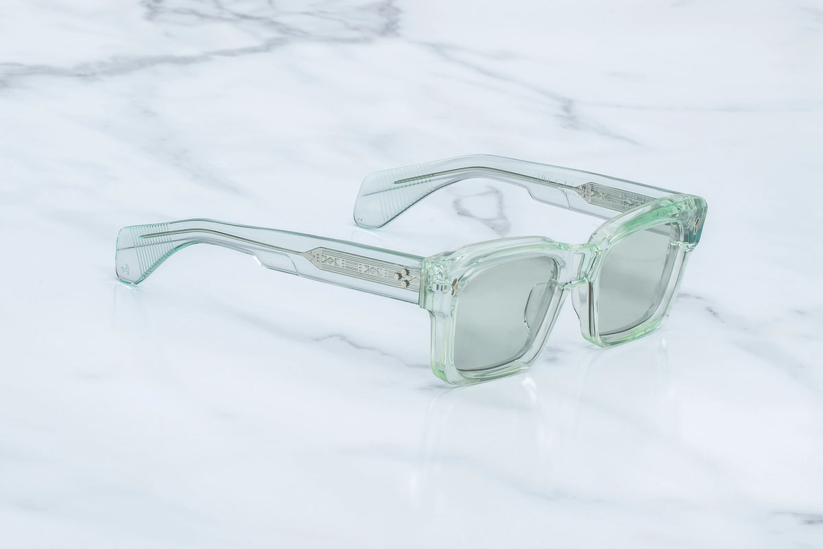 Three-quarter studio shot of the Jacques Marie Mage Kaine Aurora photochromic sunglasses. The perspective highlights the substantial 10mm profile depth of the translucent green acetate frame face and its sharp, geometric contours. The photochromic green lenses catch the studio lighting, flowing smoothly into matching clear light green temples. Available at WINK Optometrists.
