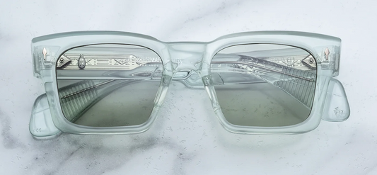 Front view of Jacques Marie Mage Kaine sunglasses from the Photochromic Collection in Aurora. The frame displays a bold, structural modified rectangular silhouette with sculpted volumes. The 10mm block acetate is a striking translucent clear light green, housing responsive photochromic bottle green lenses. Signature sterling silver arrowhead front pins decorate the upper outer corners. Available at WINK Optometrists.
