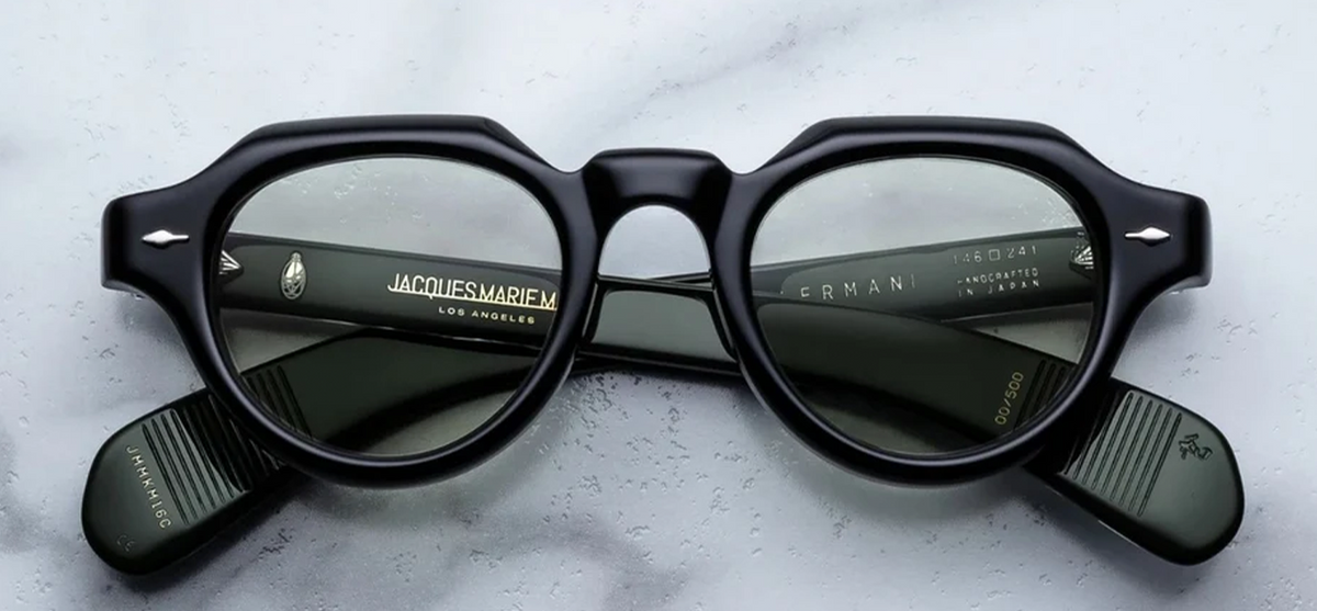 Front view of Jacques Marie Mage Kellerman eyeglasses in Cobra. The frames present a bold, sculptural, modified Panto-shape silhouette featuring a distinctively angular crown-panto top edge. Crafted from a substantial 10mm block of polished jet-black cured cellulose acetate, the face is decorated with JMM’s signature sterling silver arrowhead front pins at the upper outer corners. Available at WINK Optometrists.
