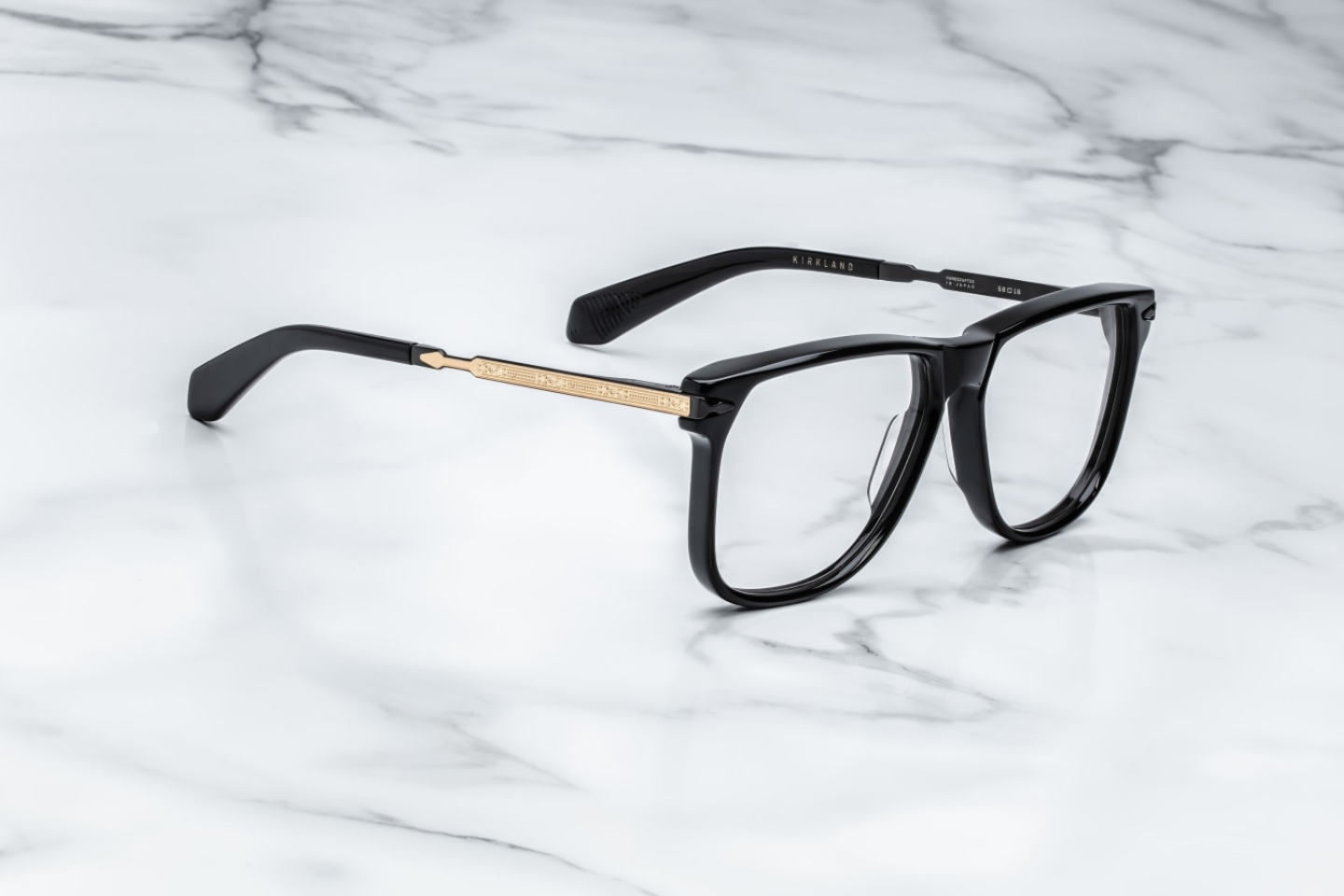 A side view of the 70's inspired boxy Kirkland frame by Jacques Marie mage with black cured acetate front, light grey lenses and dark gold 100% beta titanium temples with black accents. Available at WINK Optometrists