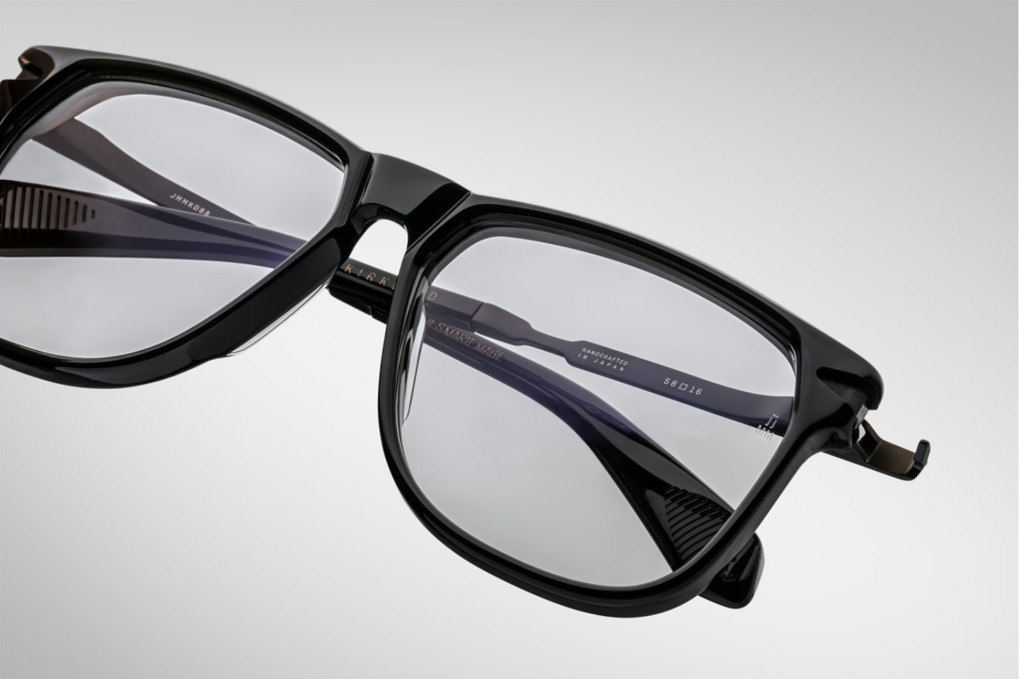 A close up view of the 70's inspired boxy Kirkland frame by Jacques Marie mage with black cured acetate front, light grey lenses and dark gold 100% beta titanium temples with black accents. Available at WINK Optometrists