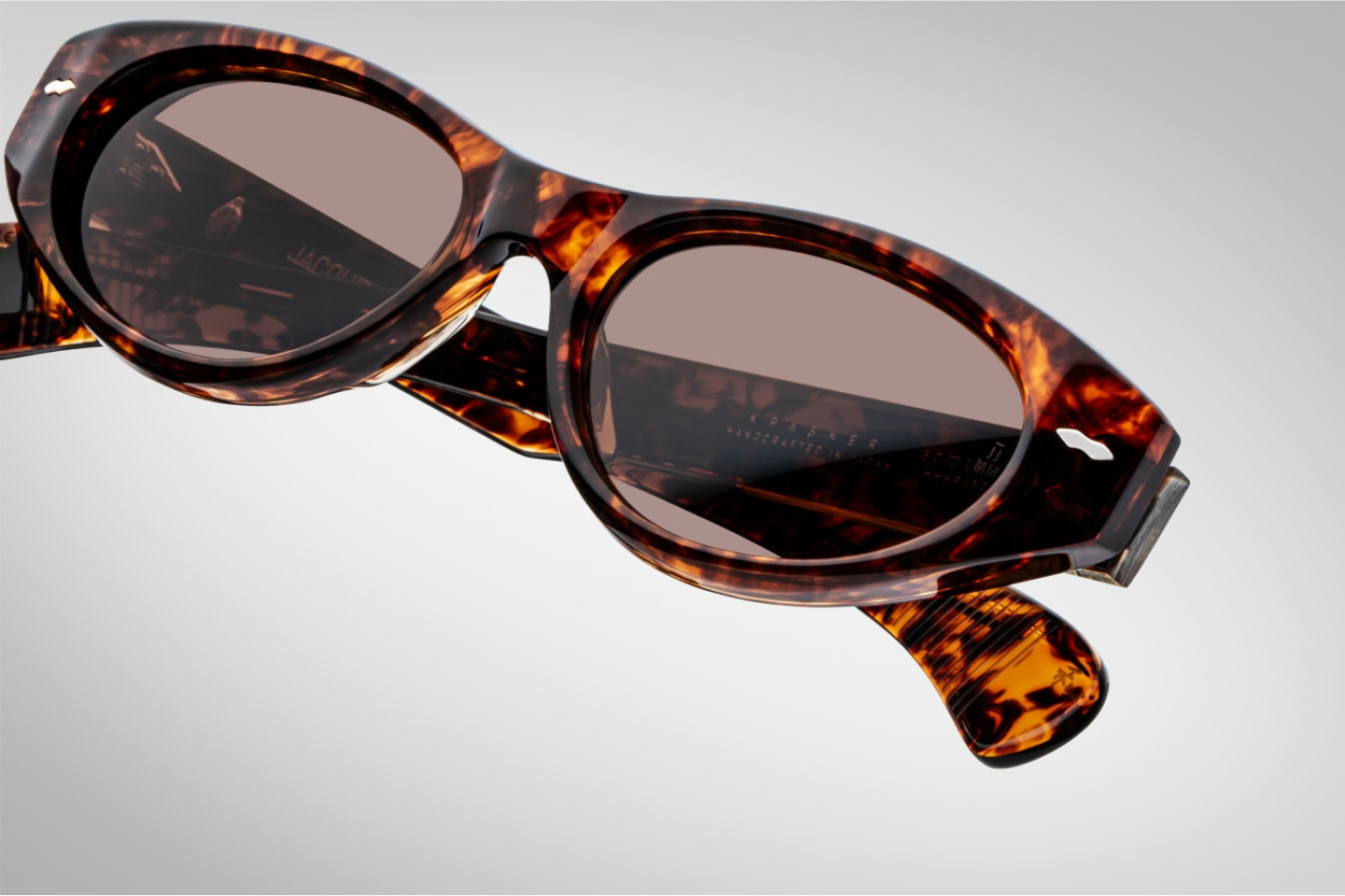 Close-up of the sienna CR39 lenses of Jacques Marie Mage Krasner sunglasses in Samoa, offering 100% UV protection and backside anti-reflective treatment. The lenses are set within a 10mm havana cured cellulose acetate frame, accented with silver double-arrowhead front pins.
