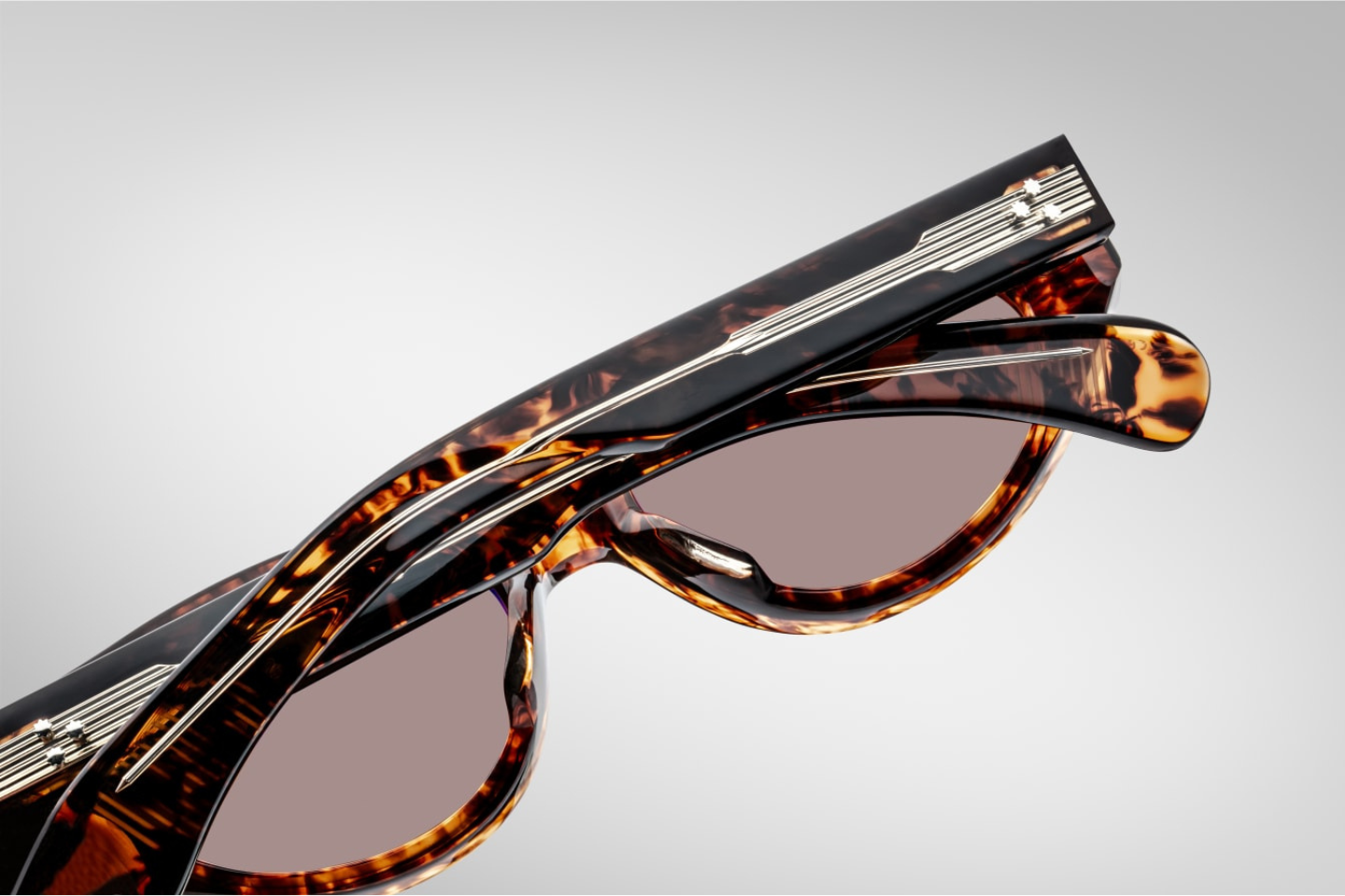 Close-up of the sienna CR39 lenses of Jacques Marie Mage Krasner sunglasses in Samoa, offering 100% UV protection and backside anti-reflective treatment. The lenses are set within a 10mm havana cured cellulose acetate frame, accented with silver double-arrowhead front pins