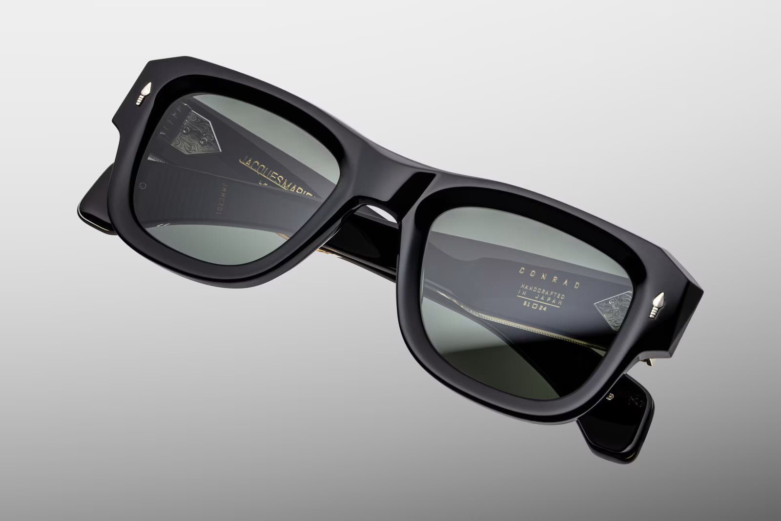Top-down view of Jacques Marie Mage Conrad Noir sunglasses. Accents the substantial 10mm thickness and architectural beveling of the black acetate frame top. The view outlines the straight, robust alignment of the clear-laminated temples and exposed gold wirecores extending back