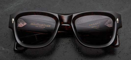 Front view of Jacques Marie Mage Conrad Beau sunglasses. Features a bold, 10mm thick Havana tortoiseshell acetate frame with an architectural, beveled square silhouette. Sterling silver signature arrowhead pins adorn the top outer corners, housing solid green-grey Stratus mineral glass lenses