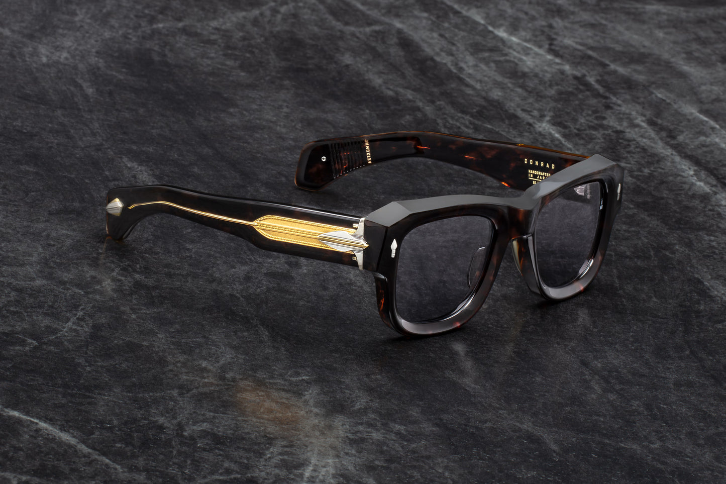 Three-quarter studio shot of Jacques Marie Mage Conrad Beau sunglasses. The angle highlights the deep beveling on the heavy Havana acetate frame and showcases the transition from the rich brown tortoiseshell front to the transparent beige temples with exposed gold cores