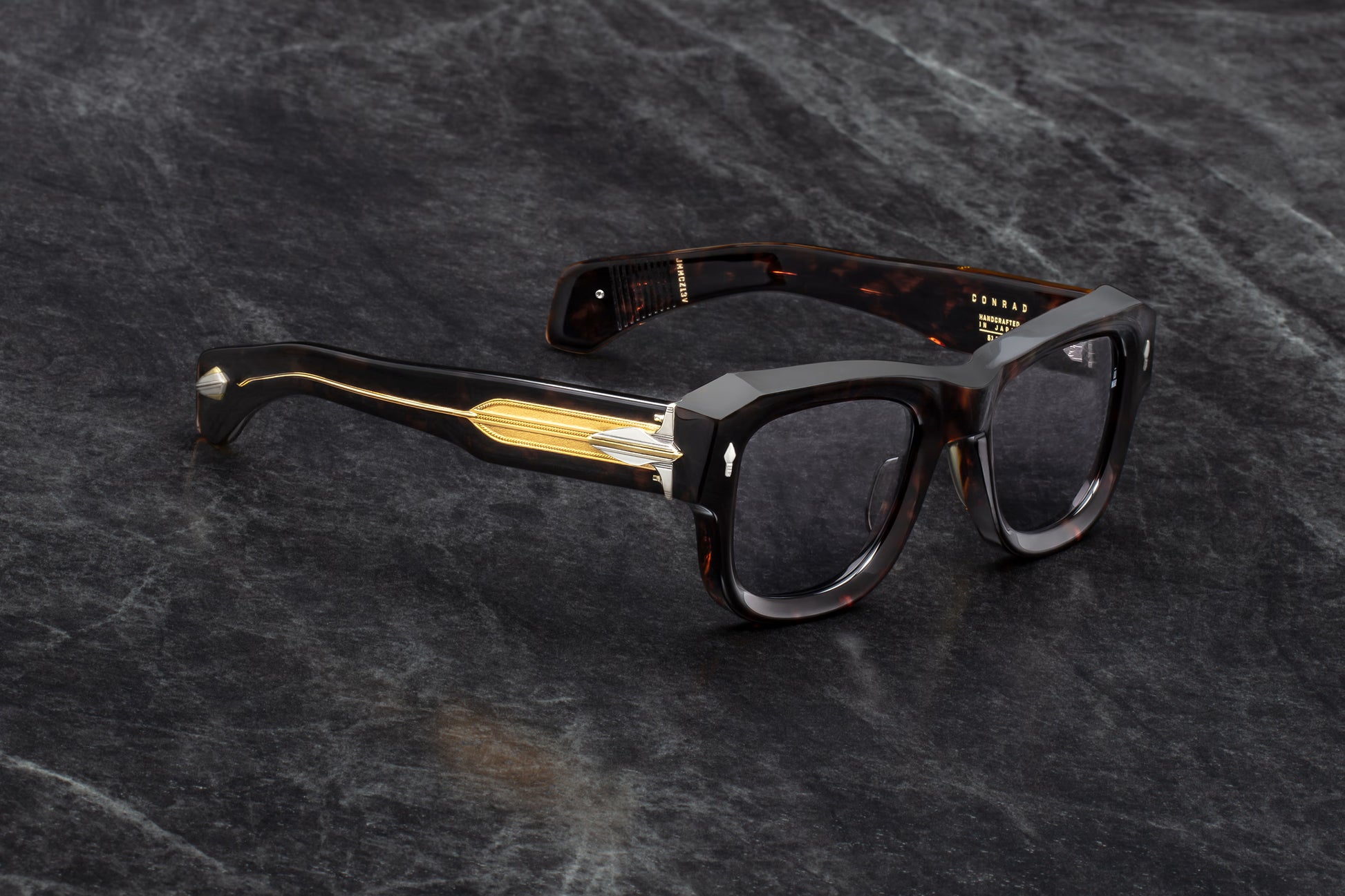 Three-quarter studio shot of Jacques Marie Mage Conrad Beau sunglasses. The angle highlights the deep beveling on the heavy Havana acetate frame and showcases the transition from the rich brown tortoiseshell front to the transparent beige temples with exposed gold cores