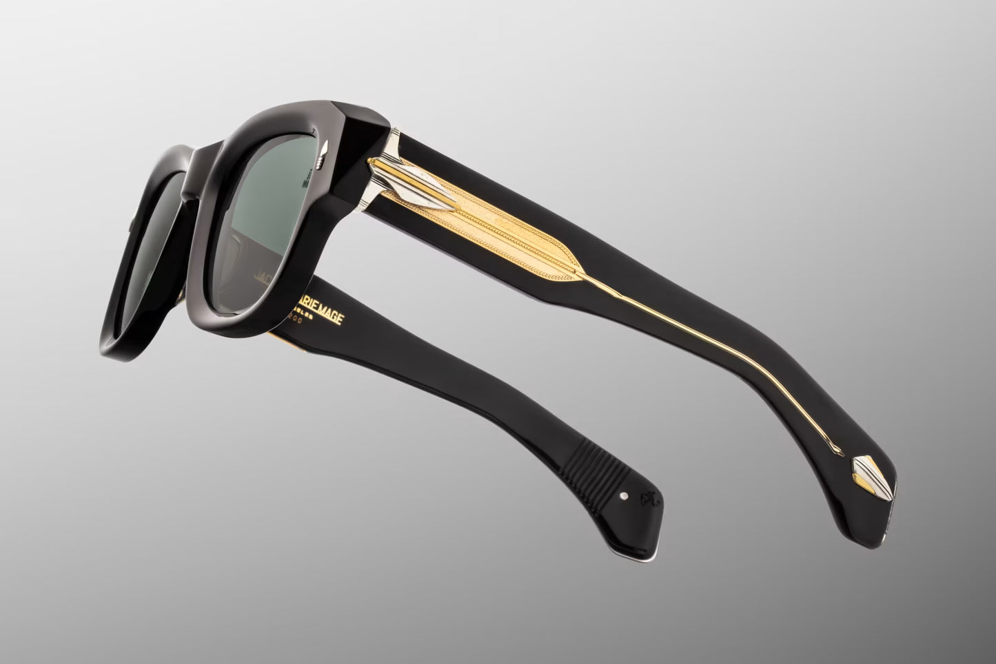 Side profile of JMM Conrad Noir sunglasses showing the double-laminated temples. The clear acetate exterior exposes an intricate, custom-braided dark gold wirecore running the length of the arm. Detailed silver palladium-plated arrowhead ornaments trim the hinge area