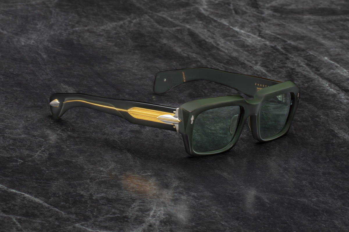 Three-quarter studio shot of Jacques Marie Mage Dakota Viper sunglasses. The angle highlights the chunky, structural beveling of the dark green acetate front frame. It captures the dramatic shift from the deep green silhouette to the transparent temple sections that reveal the metallic wirecore