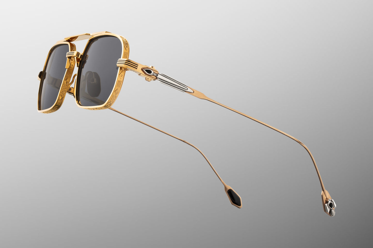 Side profile of JMM Deaver Maxi sunglasses highlighting the detailed temples. The dark gold beta-titanium temple arms feature dual-tone sterling silver arrowhead hardware inlaid with hand-shaped black onyx gemstones. The arms are secured by custom silver palladium monoblock hinges