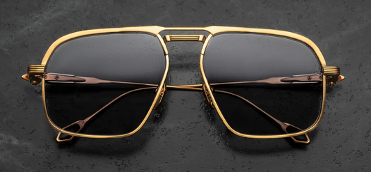 Front view of Jacques Marie Mage Labarge Maxi sunglasses. Features a large 1970s-inspired dark gold titanium navigator frame with a thick monoblock top bar and silver palladium accents. The eye rims display fine Chimayo textile engravings and hold solid grey armorlite lenses