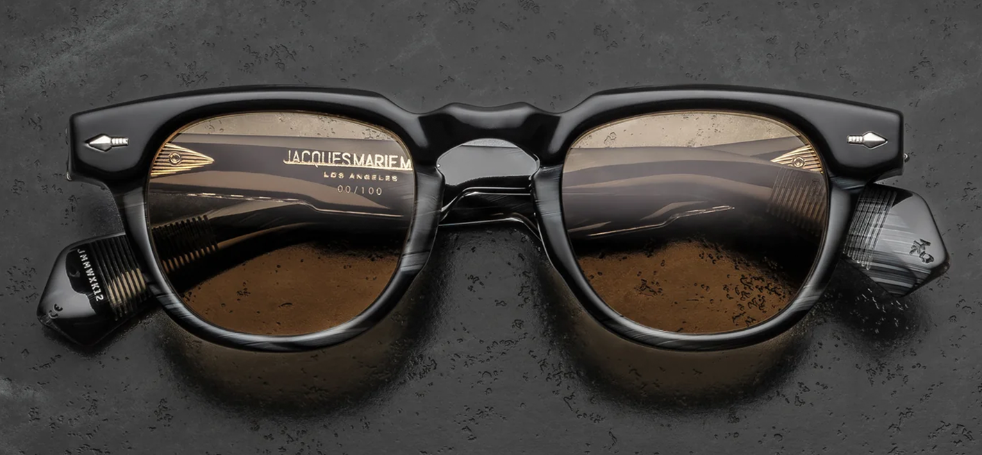 Front view of Jacques Marie Mage Wahkan Ridgeway sunglasses. Features a chunky, 10mm thick rounded acetate frame in polished black horn with a distinctive dimpled keyhole bridge. Displays a black-and-brown laminated brow bar accent and signature sterling silver arrowhead front pins, housing warm honey-coloured lenses