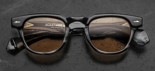 Front view of Jacques Marie Mage Wahkan Ridgeway sunglasses. Features a chunky, 10mm thick rounded acetate frame in polished black horn with a distinctive dimpled keyhole bridge. Displays a black-and-brown laminated brow bar accent and signature sterling silver arrowhead front pins, housing warm honey-coloured lenses