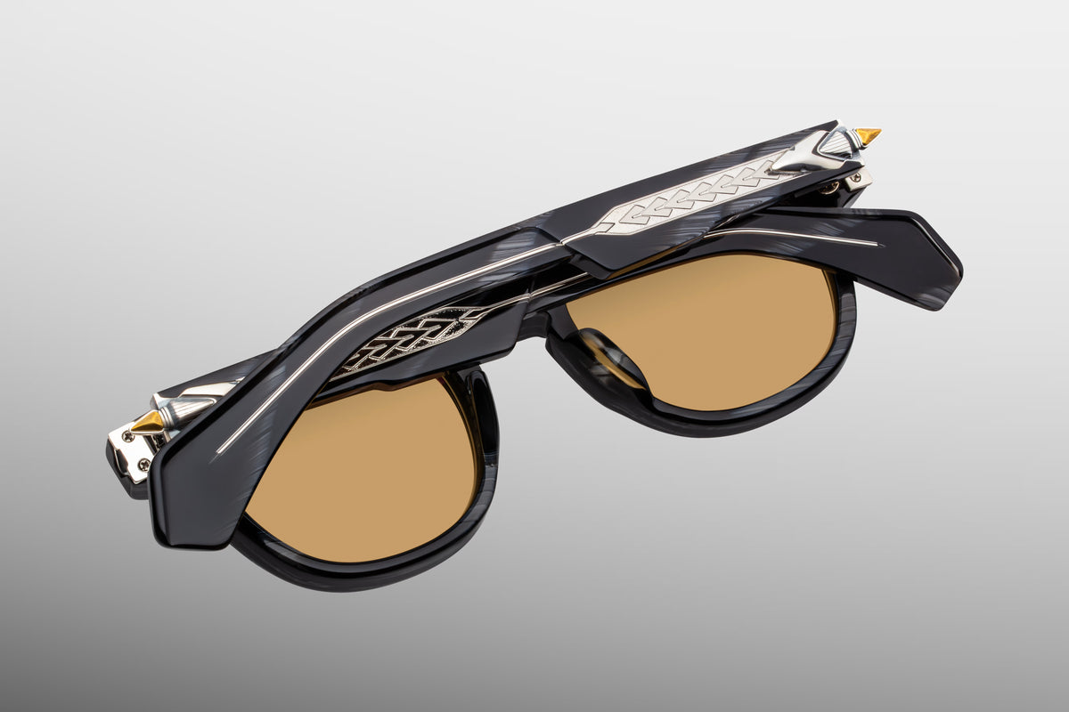 Side profile of JMM Wahkan Ridgeway sunglasses showing the ornate temple arms. The custom double-laminated temples feature a clear acetate exterior exposing an intricate, engraved silver palladium "Pathfinder" wirecore with brass details. Embellished with sterling silver arrowhead accents near the custom monoblock hinge
