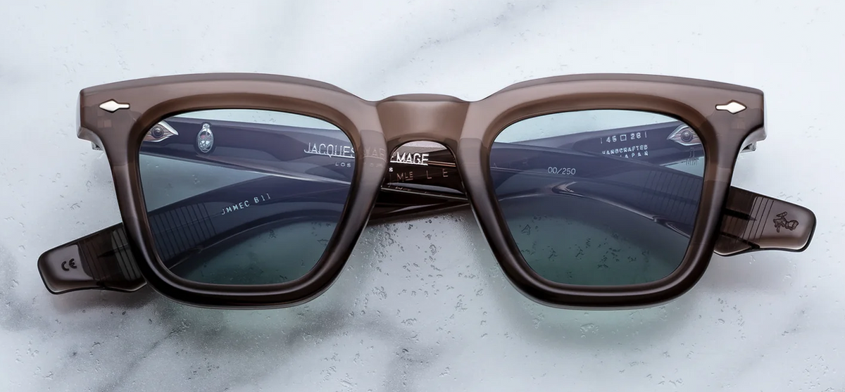 • 
A front-facing product shot of Jacques Marie Mage Leclair sunglasses in Dusty Jade. The frame features a bold, sharp 1950s-inspired Wellington silhouette crafted from semi-transparent, taupe-toned cellulose acetate. The vibrant grove-green lenses are framed by a thick, structured bridge, accented by signature silver arrowhead pins positioned horizontally on the upper outer corners of the frame front.
