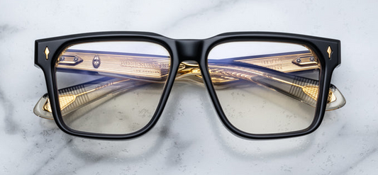 front view of Jacques Marie Mage Lucknow Beluga glasses. The bold rectangular frame is 10 mm thick with sculpted volume cuts and a flat browline. At each hinge front, a polished light-gold sterling arrowhead pin adds Art Deco flair. The lenses are super-light bronze-tinted CR39 with backside anti-reflective coating and full UV protection.