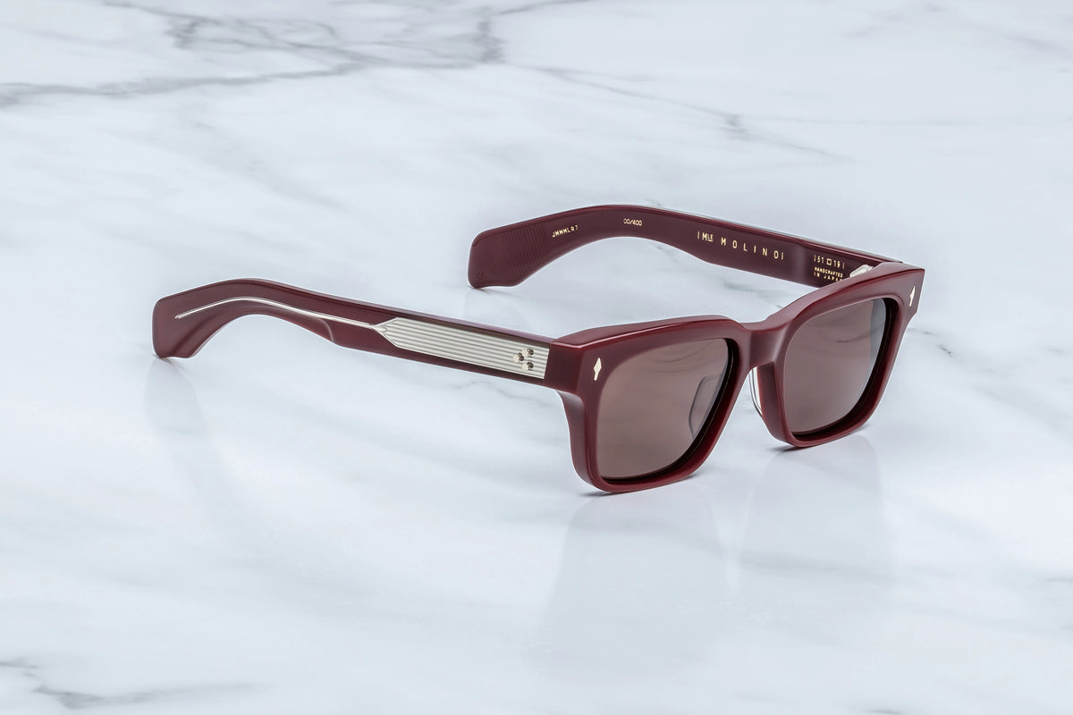 Three-quarter view of the Jacques Marie Mage Molino Bordeaux Empire sunglasses. The angle captures the heavy frame volume and subtle hand-polished brow beveling, transitioning into thick, dual-layered temples that reveal a silver filigree wire core through clear outer acetate.