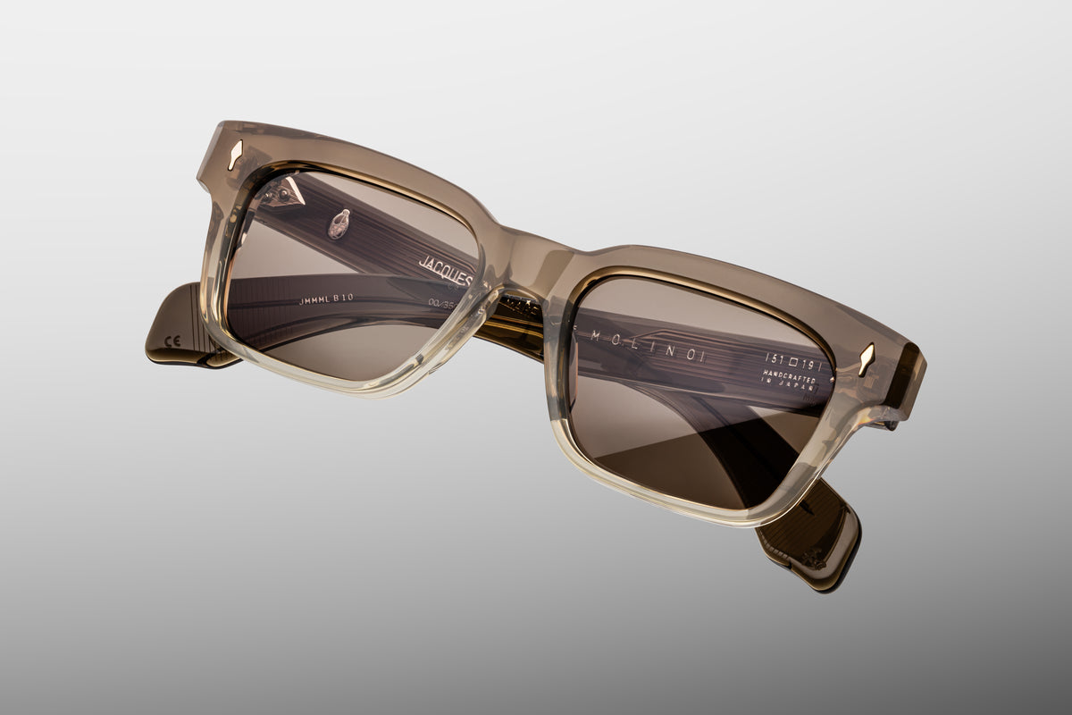 Extreme close-up of the front corner of Jacques Marie Mage Molino Lescot sunglasses, highlighting the pristine gloss of the rich brown acetate frame, smooth beveled contours, and a flush-mounted sterling silver arrowhead accent pin.
