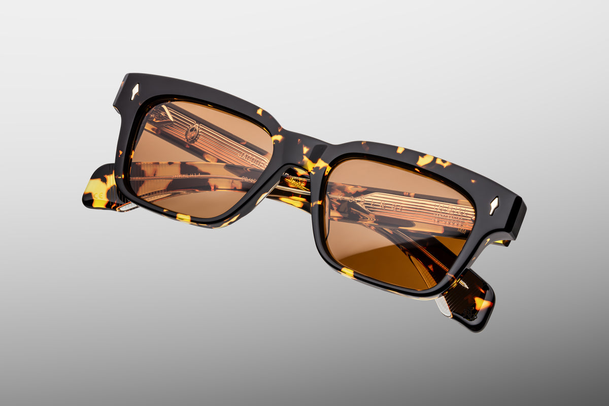Extreme close-up of the front corner of Jacques Marie Mage Molino Tokyo sunglasses. Captures the high-gloss polish of the amber-flashed tortoiseshell acetate, the sharp bevel contours, and a flush-mounted sterling silver arrowhead accent pin.