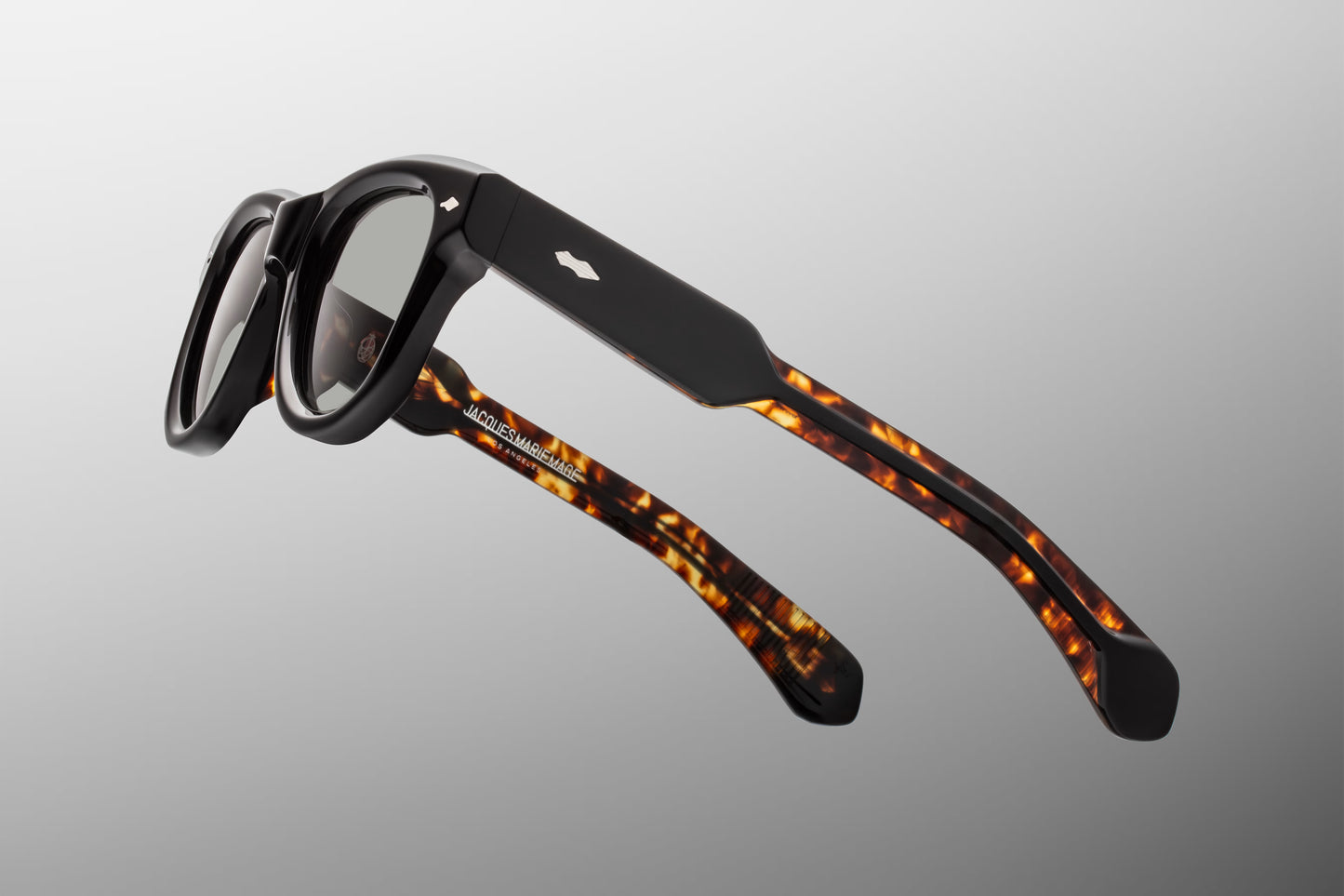 Side view of the JMM Kinshasa sunglasses temple arm, highlighting the dual-laminated black and tortoise acetate structure and the exposed sterling silver wirecore with engraved Art Deco details