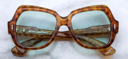 A pair of Jacques Marie Mage sunglasses with a camel brown patterned frame, displayed on a surface.
