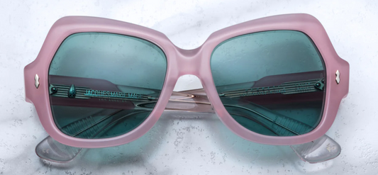 Head‑on view of Perreti Daisy: oversized, sculptural round‑panto eyeglasses in soft translucent pastel pink acetate. The thick 10 mm full‑rim frame surrounds green-tinted CR‑39 demo lenses. A defined saddle keyhole bridge centers the design, and light‑gold double arrowhead pins are inset at the upper outer corners.