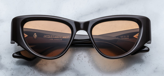 Jacques Marie Mage Seymour sunglasses in Walnut, featuring a medium-sized cat-eye silhouette with a soft wrap-around design, arched brow, and V-shaped bridge. The frame is crafted from 10mm polished cured cellulose acetate in a rich walnut hue, accented with dark gold metal embellishments and orange CR39 lenses