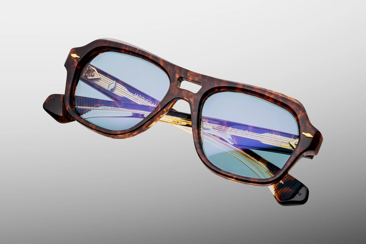 Extreme close-up of the front chassis on Jacques Marie Mage Tamerlis sunglasses. Captures the high-gloss polished finish of the thick acetate, the complex multi-angled beveling along the arched brow, and a flush-mounted signature arrowhead pin.