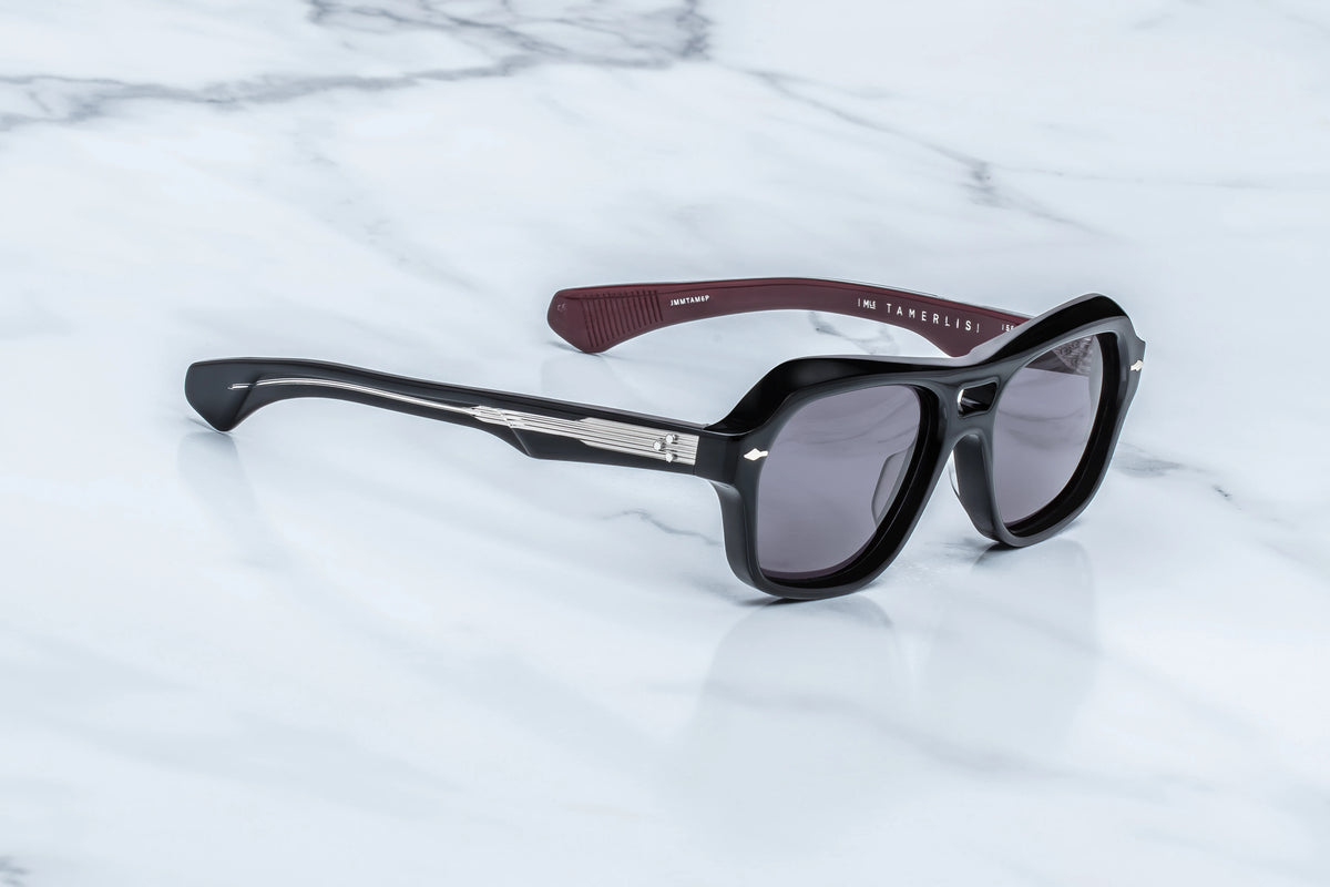 Three-quarter view of the Jacques Marie Mage Tamerlis Bloodstone sunglasses. The angle highlights the deep contouring across the dual bridge and the triple-laminated temples, showing the transition from the black frame front to a clear-coated arm that reveals internal silver detailing.