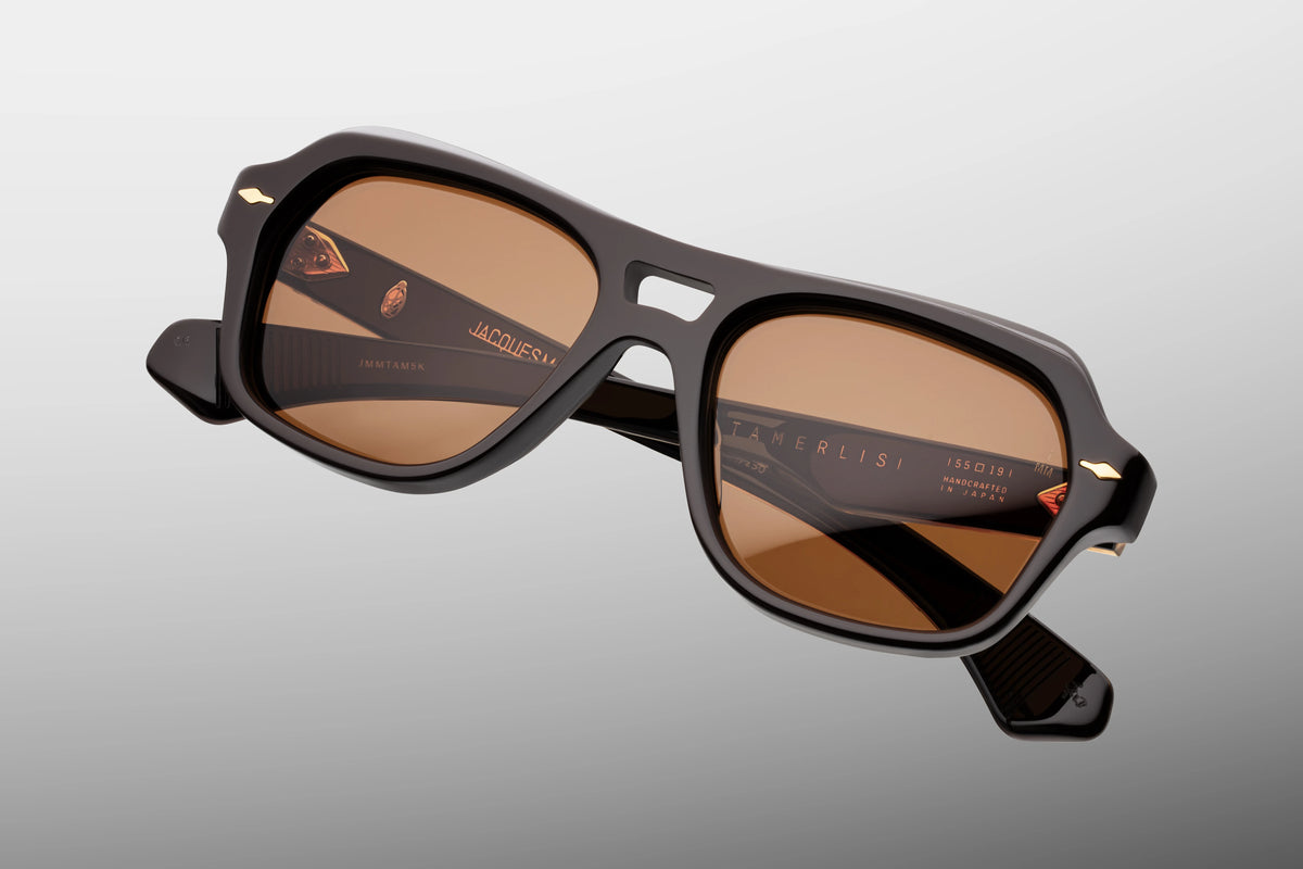 Extreme close-up of the front chassis of Jacques Marie Mage Tamerlis Walnut sunglasses. Captures the high-gloss shine of the rich brown acetate, the sharp multi-angled contouring across the double bridge, and a flush-mounted dark gold arrowhead pin.