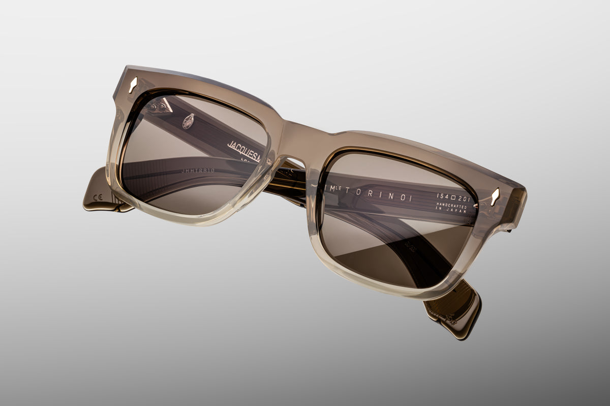  Extreme close-up of the front corner of Jacques Marie Mage Torino Lescot sunglasses. Captures the high-gloss shine of the warm brown acetate frame, smooth beveled contours, and a flush-mounted sterling silver arrowhead pin.