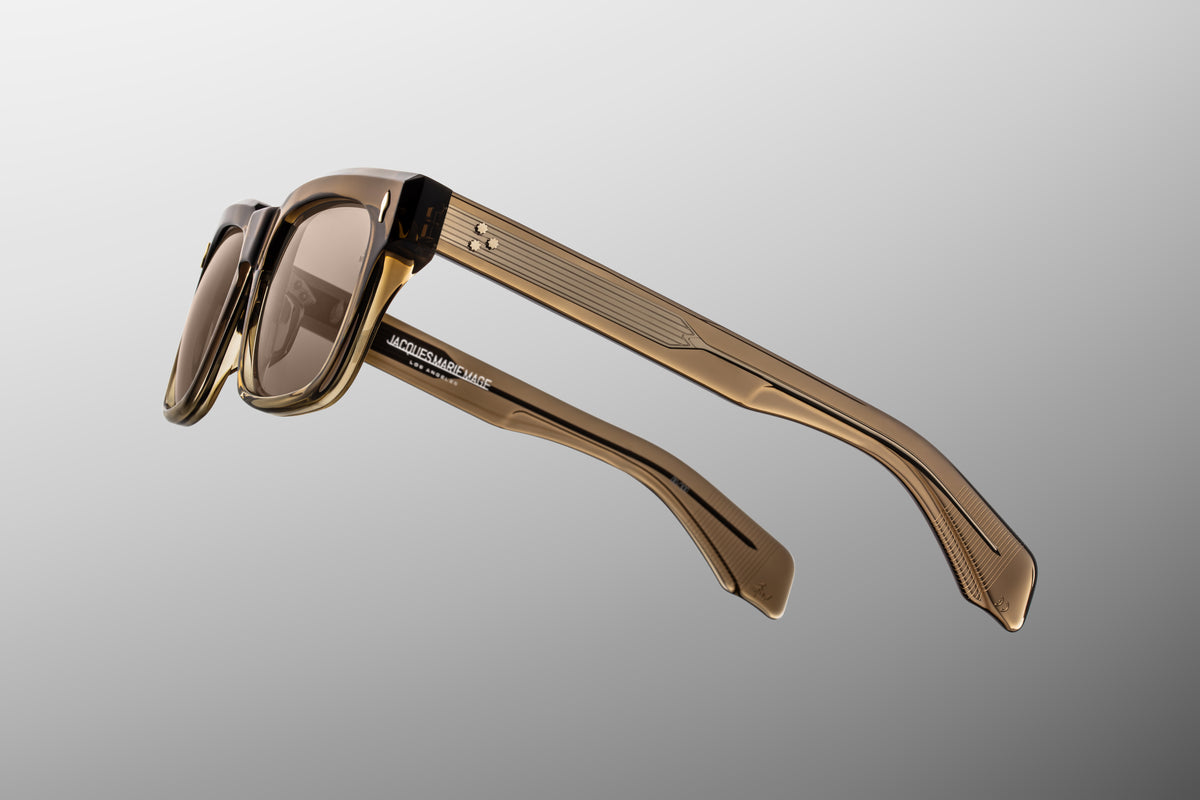 Macro shot of the temple arm on Jacques Marie Mage Torino Lescot sunglasses. The crystal-clear exterior laminate layer provides a window to the exposed silver palladium wire core engraved with intricate Art Deco filigree.