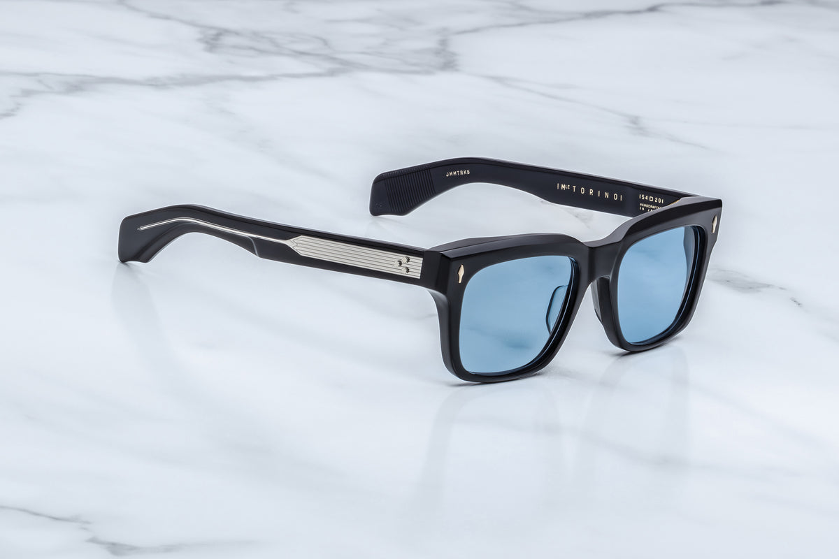  Three-quarter view of the Jacques Marie Mage Torino Obscure sunglasses. This angle showcases the frame's structural volume, hand-polished angular beveling along the brow line, and thick temples that reveal a gold wire core through a clear inner laminate layer.