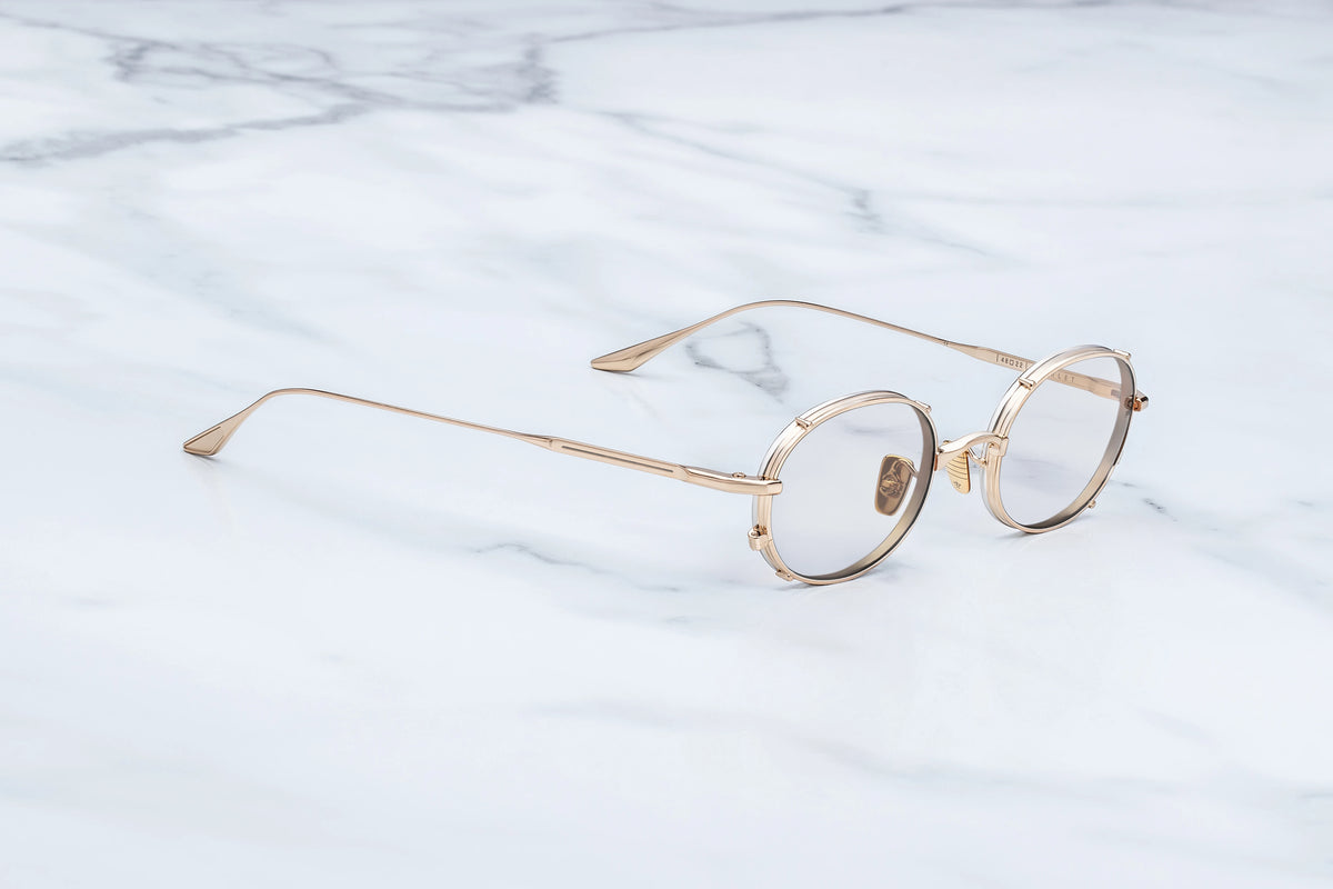 Side profile view of the Jacques Marie Mage Violet RX Darjeeling glasses. The sleek, ultra-thin gold titanium temple arms run straight back, showing off a featherlight design. The slender arms cleanly transition into custom sculpted, signature winged temple tips finished with hand-painted translucent brown epoxy detailing.