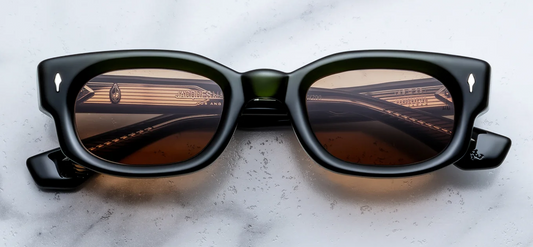 A front-facing product shot of Jacques Marie Mage Whiskeyclone sunglasses in the Bornéo colourway. The 90s-inspired, low-profile rectangular frame is crafted from thick 10mm polished translucent forest green acetate. Vibrant, solid orange lenses are encased in the heavy rim, accented by signature sterling silver arrowhead pins positioned horizontally on the upper corners.
