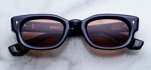 A front-facing product shot of Jacques Marie Mage Whiskeyclone sunglasses in the Minuit colourway. The 90s-inspired, low-profile rectangular frame is sculpted from thick 10mm polished translucent midnight blue acetate that appears nearly black. Warm, reddish-brown Sherry CR39 lenses are nestled within the frame, flanked by horizontal sterling silver arrowhead pins on the upper corners
