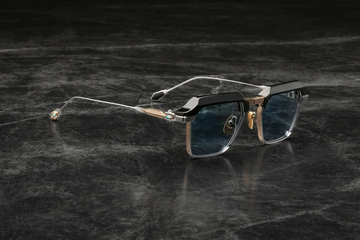 A three-quarter angle showcasing the profile of the luxury eyewear. The glossy black acetate top bar seamlessly integrates into silver beta titanium temples. Near the hinge, a prominent, sculptural 18k gold-plated arrowhead motif stands out sharply against the silver metal.