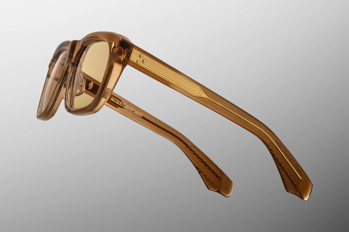 Side profile view of the Jacques Marie Mage Yves from the Photochromic Collection in Solaris. The focus is on the thick, custom double-laminated temple arms featuring Clear Beige exteriors combined with rich Whiskey Crystal interiors. A premium, custom Dark Gold tension-secured 7-barrel hinge securely fastens the heavy temple arm to the translucent front frame face. Available at WINK Optometrists.