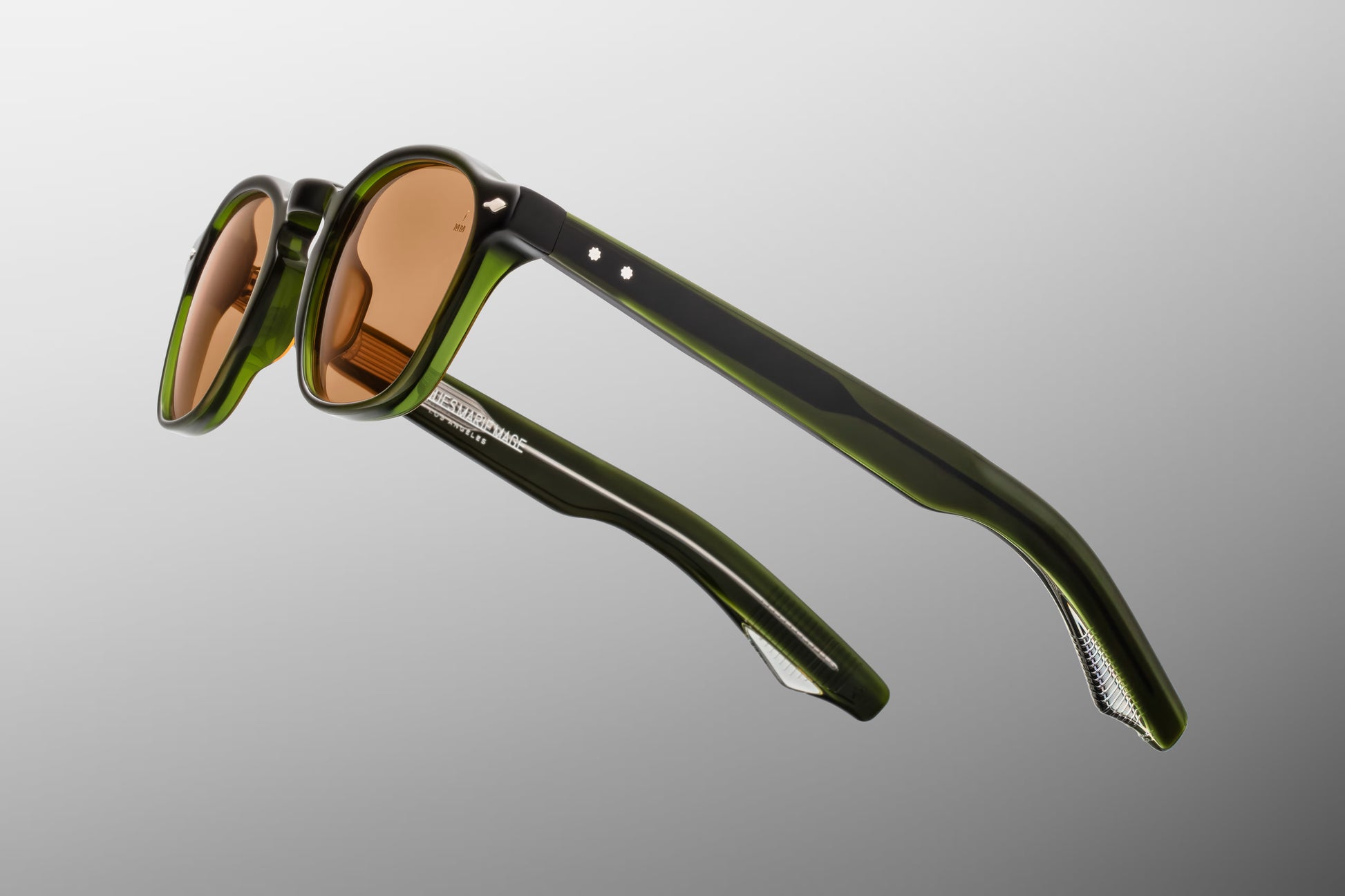 Side view of the JMM Zephirin Borneo sunglasses temple arm, showcasing the glossy green double-laminated acetate construction and the signature flush sterling silver spur-shaped rivets.