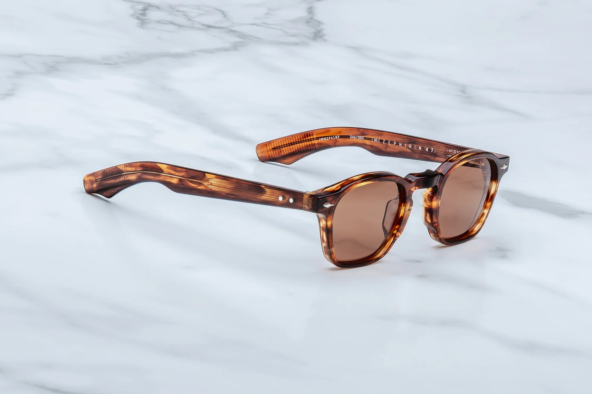 Three-quarter angled studio shot of the JMM Zephirin Bourbon sunglasses, highlighting the retro keyhole bridge, distinct sculptural 10mm frame bevels, and warm amber-brown tortoise shell tones.