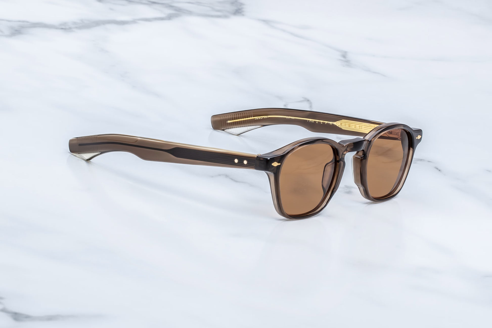 Three-quarter angled studio shot of the JMM Zephirin London sunglasses, highlighting the structural beveling of the thick 10mm frame and the rich, honey-toned translucency of the brown acetate.