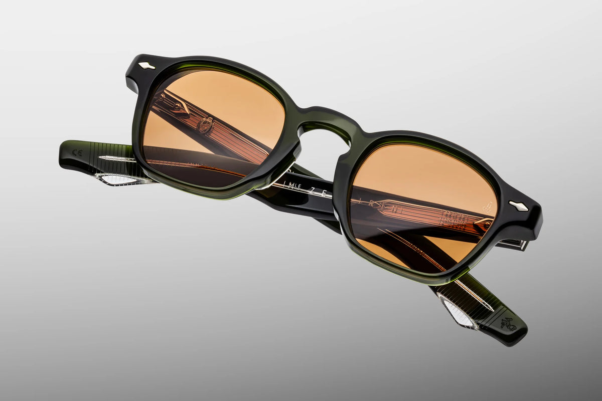 A detailed, close-up front studio shot of the Jacques Marie Mage Zephirin sunglasses in the Borneo colorway. The thick, sculpted rectangular frame is made of deep, translucent bottle-green 10mm cellulose acetate, contrasting with bold, vibrant solid orange CR39 lenses. Prominent silver precious-metal arrowhead pins sit flush at the outer upper corners of the frame, and the keyhole bridge architecture is clearly visible at the centre