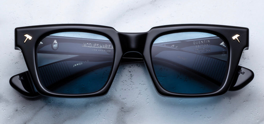 Jacques Marie Mage Johnny Cash Quentin sunglasses—limited edition eyewear inspired by Cash's 1969 San Quentin concert. Features hatchet-shaped front pins, paddle temples, and signature 'Johnny Cash' foil marking. Handcrafted in Japan with black double-laminated 10mm cured cellulose acetate frame and temples, silver tension-secured 9-barrel hinges, and sweet brown CR39 lenses offering 100% UV protection and backside anti-reflective treatment