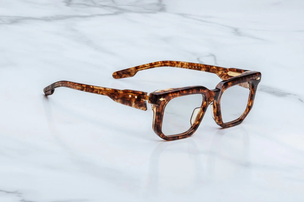 Three-quarter studio shot of the Jacques Marie Mage Argyle eyeglasses. The angled perspective highlights the substantial profile depth of the thick tortoiseshell rims and the hand-sculpted contours of the frame face. The clear demo lenses transition seamlessly into the custom double-laminated temples. Available at WINK Optometrists.