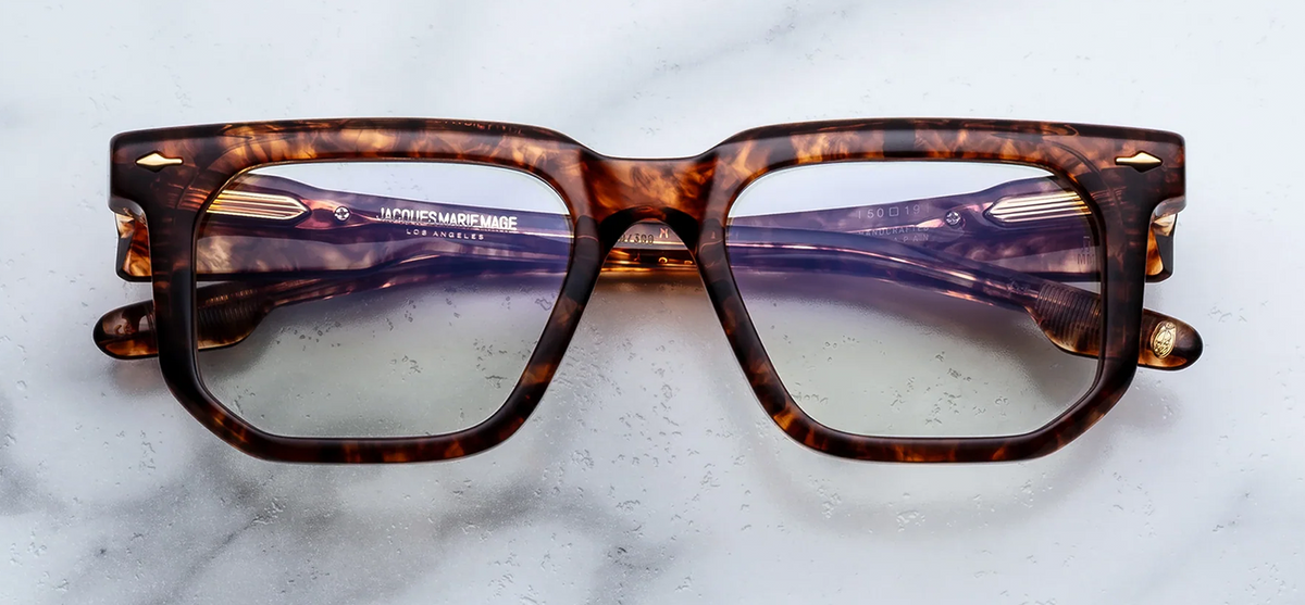 Front view of Jacques Marie Mage eyeglasses in Argyle. The heavy 10mm cured cellulose acetate frame showcases a rich Havana tortoiseshell pattern with mottled dark brown, amber, and translucent spots. Signature dark gold arrowhead front pins decorate the upper outer corners of the bold frame face. Available at WINK Optometrists.