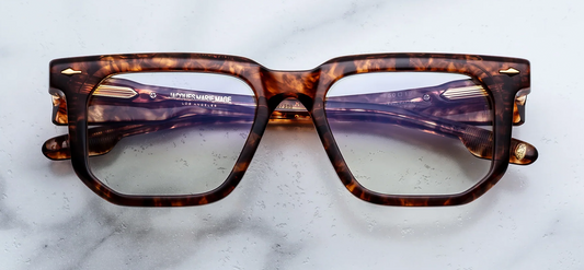 Front view of Jacques Marie Mage eyeglasses in Argyle. The heavy 10mm cured cellulose acetate frame showcases a rich Havana tortoiseshell pattern with mottled dark brown, amber, and translucent spots. Signature dark gold arrowhead front pins decorate the upper outer corners of the bold frame face. Available at WINK Optometrists.