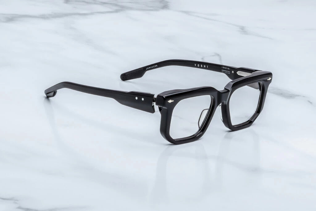 Three-quarter studio shot of the Jacques Marie Mage Yoshi Black RX frames. The perspective showcases the heavy profile depth of the glossy black geometric frame face and its cleanly sculpted, architectural edges. The clear demo lenses highlight the structural thickness of the rims, transitioning smoothly into bold, sculptural black acetate temples. Available at WINK Optometrists.
