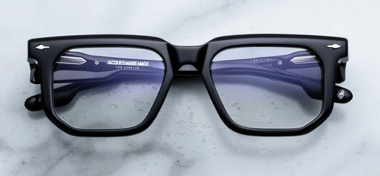 Front view of Jacques Marie Mage Yoshi RX eyeglasses in Black. The frame exhibits a distinctive, low-profile geometric silhouette with sharp, angular corners and a straight top brow. Crafted from a substantial block of high-gloss, deep lacquered jet-black cured cellulose acetate, the face is decorated with signature sterling silver arrowhead front pins at the outer corners. Fitted with clear demo lenses. Available at WINK Optometrists.
